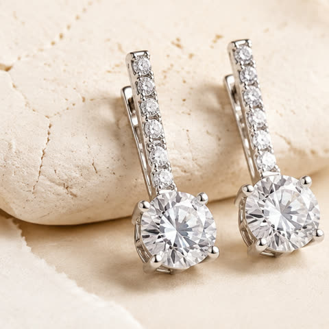 A pair of diamond drop earrings on pale stone.