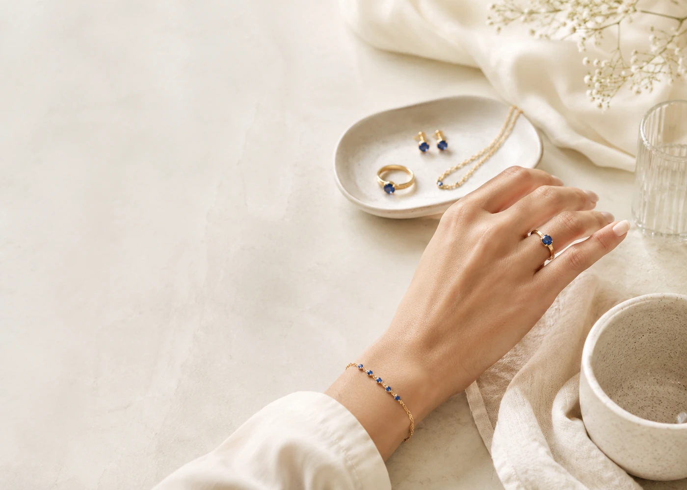 A hand wearing blue gemstone jewelry beside a tray of coordinating pieces in a calm daily setting.