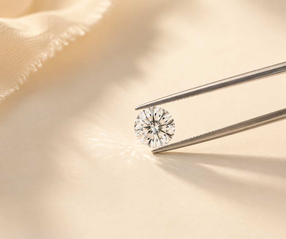 A loose round diamond held carefully with jewelry tweezers in warm natural light.
