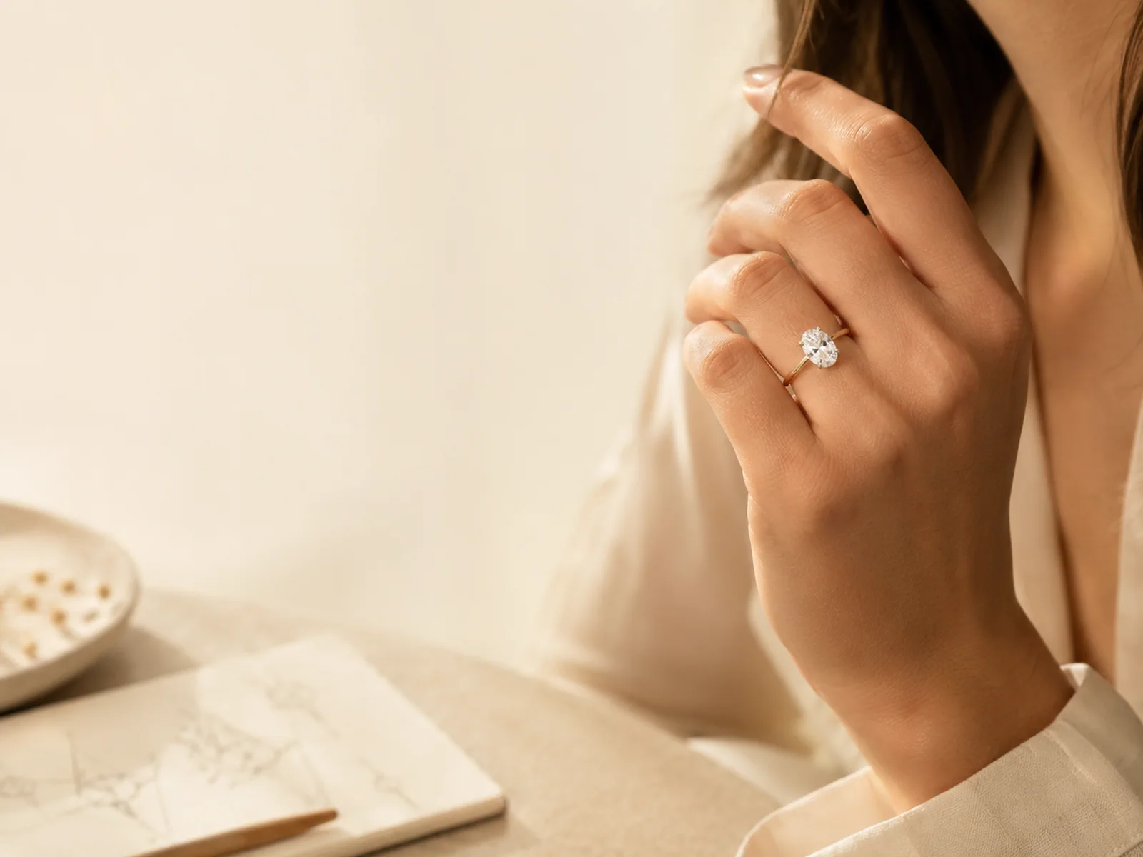 Woman wearing an oval solitaire engagement ring beside a jewelry sketchbook.