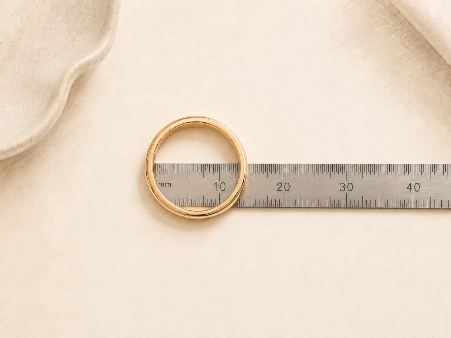 A ring lying flat with a millimeter ruler measuring the widest inside diameter from inner edge to inner edge.